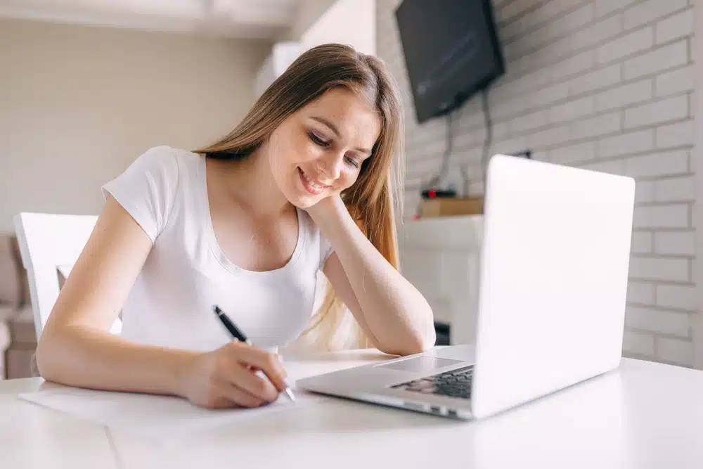Une personne concentrée, lisant des documents scientifiques et prenant des notes sur un ordinateur portable, symbolisant un projet de recherche en cours.